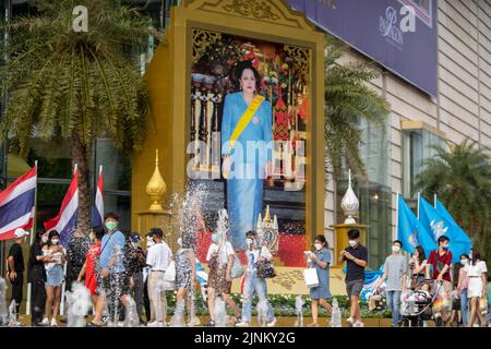 Bangkok, Thailand. 12. August 2022. Vor dem berühmten Einkaufszentrum Siam Paragon in Bangkok kommen die Menschen an einem großen Porträt der Königlichen Hoheit, der Königin Sirikit, vorbei. Die Königin Mutter von Thailand, Königliche Hoheit Königin Sirikit, feierte ihren 90.. Geburtstag. Ihr verstorbener Ehemann, HRH, König Bhumibol, regierte über 70 Jahre, der längste aller Könige in der thailändischen Geschichte und der drittlängste der Welt. Die Mutter des heutigen Monarchen, König Vajiralongkorn, die Königin Mutter, litt unter Krankheit und hat in letzter Zeit keine öffentlichen Auftritte gemacht. (Bild: © Adryel Talamantes/ZUMA Press Wire) Stockfoto