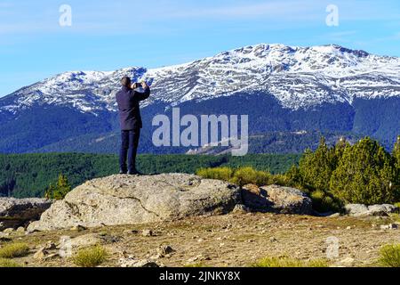 Der Mann kletterte auf einen Felsen und machte mit seinem Handy Fotos in die Berge. Morcuera Madrid. Stockfoto