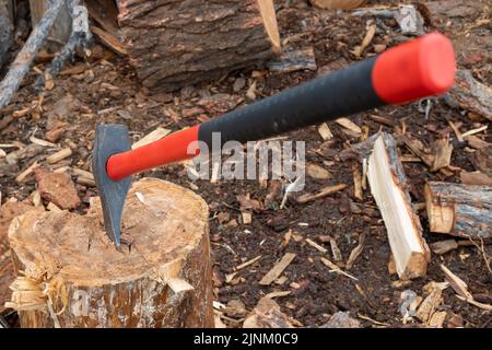 Ein Blick auf ein großes Spaltstück, eine Axt mit einem Kunststoff-, Gummigriff, der in einem Keil festgeklebt ist, ein Baumstamm Stockfoto