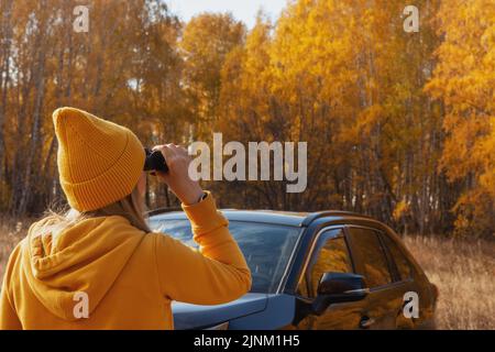 Eine schöne positive Frau in gelber Kleidung mit Fernglas bei einem Picknick an einem Herbsttag. Das Konzept der Straße, Freiheit, Ruhe, Reisen Stockfoto