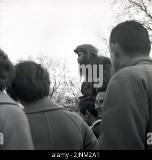 1960s, historische Menschen, die einem jungen Mann mit langem Bart zuhören und eine Mütze an den Rednercorner's im Londoner Hyde Park, London, England, Großbritannien, wetern. Stockfoto