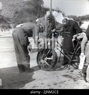 1960, historisch, am Straßenrand, ein Mann in Overalls und einer Kappe, der Motoröl in den Motor auf dem Vorderrad eines alten motorisierten Fahrrads einsetzte, der an der Veteranenwagenfahrt von London nach Brighton, East Sussex, England, Großbritannien, teilnahm. Das Kennzeichen des Motorrads ist BKE 75. Stockfoto