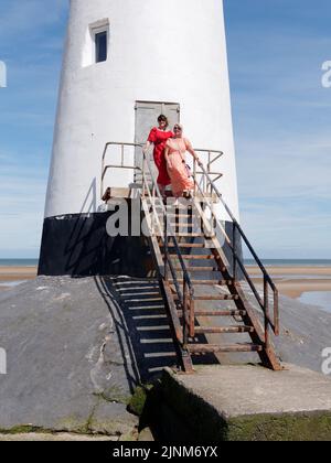 Elegant gekleidete Frauen am Point of Ayr Lighthouse alias Talacre Lighthouse, einem denkmalgeschützten Gebäude am Strand. Wales. Stockfoto