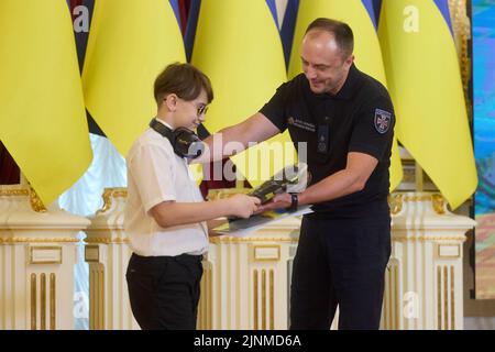 Kiew, Ukraine. 12. August 2022. Serhiy Kruk, Leiter des ukrainischen Staatlichen Notdienstes, gratuliert dem 10-jährigen Maxim Brovchenko, der am 12. August 2022 in Kiew, Ukraine, bei einer Veranstaltung zur Feier von Kinderrettern und Kriegshelden am Internationalen Jugendtag in der Weißen Halle der Helden im Mariinskyi-Palast, links war. Maxim zeichnet Raumbilder und verkauft sie, um anderen zu helfen. Quelle: Sarsenov Daniiar/Ukraine Presidency/Alamy Live News Stockfoto