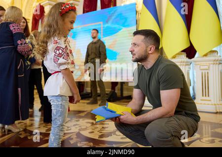 Kiew, Ukraine. 12. August 2022. Der ukrainische Präsident Wolodymyr Zelenskyy spricht mit der 7-jährigen Irynka Vasilyeva, die am Internationalen Jugendtag im Weißen Heldensaal des Mariinskyi-Palastes am 12. August 2022 in Kiew, Ukraine, Kinderretter und Kriegshelden feiern wird. Irynka Vater wurde bei der russischen Invasion getötet, und sie macht jetzt Blumenkronen und verkauft sie, um Waffen für die ukrainische Armee zu kaufen. Quelle: Sarsenov Daniiar/Ukraine Presidency/Alamy Live News Stockfoto