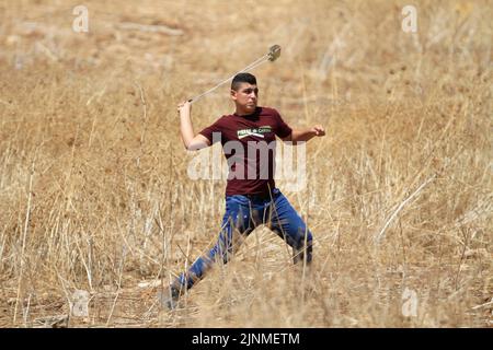 Nablus, Westjordanland, Palästina. 2. August 2022. Ein palästinensischer Protestler schleudert Steine auf die israelischen Soldaten während der Demonstration gegen israelische Siedlungen im Dorf Beit Dajan in der Nähe der Stadt Nablus im Westjordanland. (Bild: © Nasser Ishtayeh/SOPA Images via ZUMA Press Wire) Stockfoto