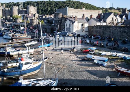 Touristen, Besucher und Fischer auf der Lower Gate Street und dem Hafen in Conwy, North Wales, mit Blick auf das Schloss im Hintergrund Stockfoto