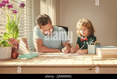 Bärtiger Vater schreibt Schulaufgaben mit seinem Jungen Sohn im Klassenzimmer, Hausaufgaben Stockfoto