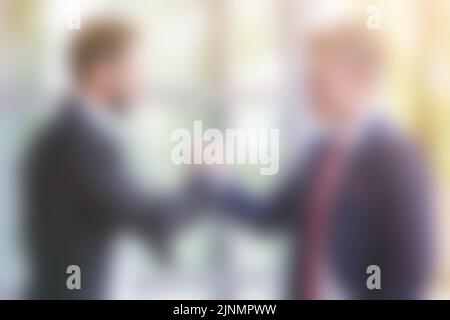 Verschwommener Hintergrund mit zwei Geschäftsleuten, die sich die Hände schüttelten Stockfoto
