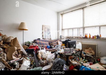 Ein dreckiges Wohnzimmer mit viel Unordnung in einem Apartment eines Hoarders. Dieses Gebäude wurde seitdem abgerissen Stockfoto