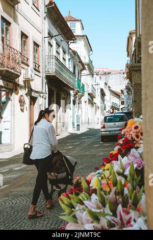 Vila Real, Portugal - 2021. September 15. - Frau, die mit einem Baby in einer schmalen Straße mit Blumen in Vila Real spazieren geht Stockfoto