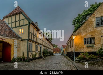 Das alte Fachwerkmuseum und die alten Häuser auf einer gepflasterten Straße in dunkles Abendlicht in Mariager, Dänemark, 7. August 2022 Stockfoto