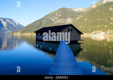 Eine hölzerne Anlegestelle führt zu einem Bootshaus am malerischen Achensee oder Achensee in den österreichischen Alpen (Österreich) Stockfoto