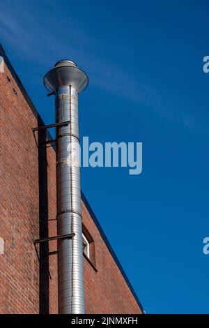 Ein silberfarbenes Auspuffrohr an einer Hauswand vor einem blauen Himmel Stockfoto