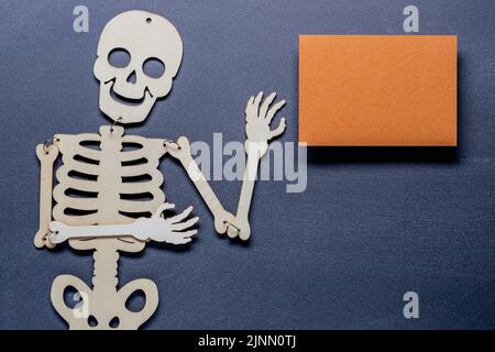 Herbst- oder Herbstzusammensetzung aus Skelett auf einem Schiefertafel-Hintergrund mit einem orangefarbenen Papierrohling. Flach liegend, Draufsicht mit Kopierplatz Stockfoto