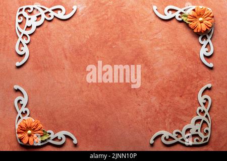 Rahmen mit Holzausschnitten und Papierblumen auf orangefarbenem texturiertem Hintergrund Stockfoto