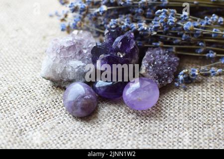 Schöne Amethyst-Steine und Amethyst-drusen mit einem trockenen Lavendelbukett vor einem Hintergrund aus grobem Sackleinen-Stoff. Magische Amulette. Stockfoto