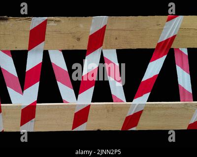 Nahaufnahme des rot-weißen Schutzbandes auf einem Holzzaun auf schwarzem Hintergrund Stockfoto