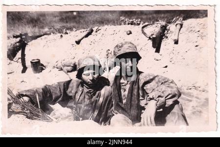 Weltkrieg zwei Wehrmachtssoldaten ruhen in einem Graben an der Russischen Front 1943 . Die Männer gehören zum Langmark-Regiment A Waffen SS-Einheit. Ihre Tarnkappen und Helmbezüge erwiesen sich als nützlich, um an der Front zu verbergen. Stockfoto