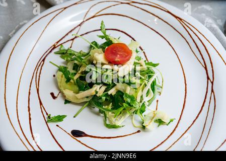 Gesunde Essenslöffel Salatsellerie und Apfelarugula mischen sich auf einem weißen flachen Teller, der mit Balsamico-Sauce auf einer grauen Stoffserviette auf dem hellen B dekoriert ist Stockfoto