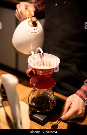 Der Barista schüttet heißes Wasser aus und macht Kaffee nach der Trichtermethode. Der Barista arbeitet hinter dem Tresen. Stockfoto