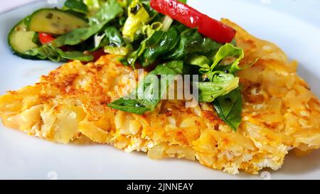 Köstliches hausgemachtes Omelett mit Ei und Kartoffeln. Darauf etwas Salat mit Tomaten und Gurke Stockfoto