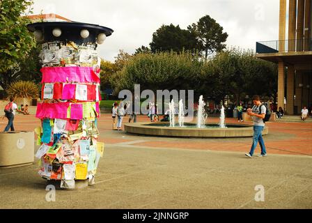 Ein männlicher Student geht durch Sproul plaza, vorbei an einem mit Flugblättern geschmückten Kiosk, als er den Campus der University of California Berkeley begibt Stockfoto