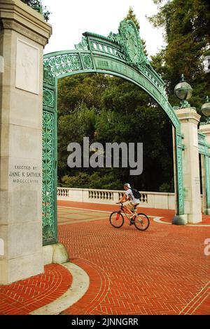 Ein junger Student fährt mit dem Fahrrad durch die historischen Sather Gates, einem Eingang zum Campus der University of California Berkeley Stockfoto