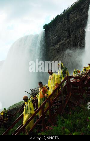 Menschen, die gelbe Poncho-Regenmäntel tragen, steigen die Treppen der Cave of the Winds Tour hinab, die Besucher zu den American Niagara Falls bringt Stockfoto