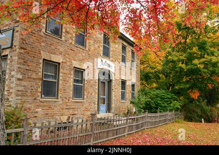 Ein Steinhaus im Herbst wird von den bunten Herbstblättern eingerahmt und ist der Ort eines Antiquitätenladens in Neu-England Stockfoto