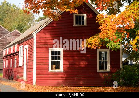 Herbstlaub und farbenfrohe Blätter umgeben ein kleines rotes Haus an einem lebhaften Herbsttag in Neuengland Stockfoto