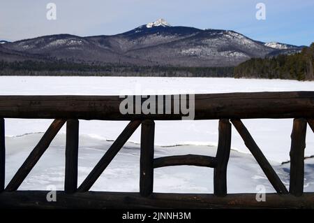 Holzstämme bilden ein Geländer auf einer Brücke, die einen kleinen Nebenfluss eines gefrorenen Sees am Fuße eines Berges in Neuengland überspannt Stockfoto