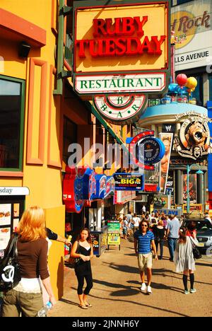 Touristen laufen entlang der Hauptgeschäftsstraße von Clifton Hill in Nagara Falls, Ontario, vorbei an kitschigen Souvenirläden und einer Vielzahl von Fast-Food-Cafés Stockfoto