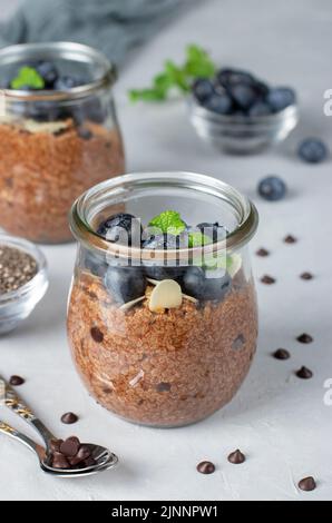 Chocolate Chia Pudding mit Heidelbeere und Mandeln in Gläsern auf grauem Hintergrund. Gesunde Ernährung Stockfoto