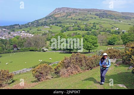 Indische Frau, die mit Llanfairfechan und Penmaenmawr Mountain in der Ferne läuft, Wales, Großbritannien Stockfoto