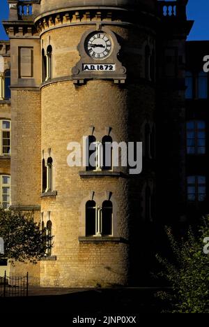 Zeit Gegenwart und Zeit Vergangenheit … Auf dem Turm, der den hoch aufragenden Schornstein der ehemaligen Bliss Tweed Mill in Chipping Norton, Oxfordshire, England, UK, stützt, überragt ein rund-um-die-Uhr-Gesicht das Datum ‘n. Chr. 1872’, dem Jahr, in dem die Mühle gebaut wurde und mit der Produktion von hochwertigen Tweedstoffen begann, die aus Cotswold- und Shetland-Wolle gesponnen und gewebt wurden. Im Ersten Weltkrieg von 1914-18 stellte sie Khaki-Tücher für die Uniformen britischer Soldaten her. Stockfoto