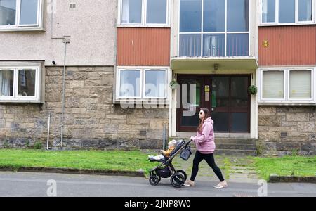 Paisley, Schottland, Großbritannien, August 7. 2022, alleinerziehende Mutter, die in armen Wohnsiedlungswohnungen mit vielen sozialen Problemen an gemeinderäten vorbeigeht Stockfoto