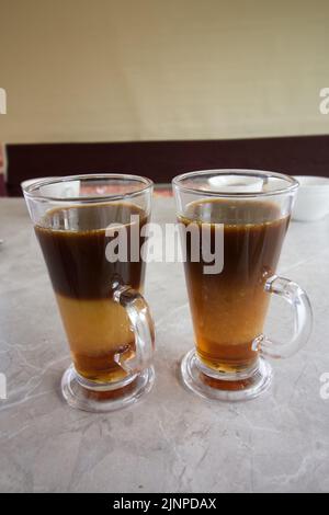 Kaffee mit Sirup und Creme. In Glaskrügen. Die Schichten des Getränks sind sichtbar. Stockfoto