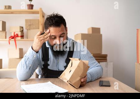 indischer männlicher Kurier, der beschädigte Schachtel, billige Paketzustellung, schlechte Versandqualität zeigt. Paket für kleine Unternehmen zum Versand. Stockfoto