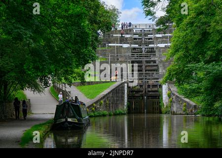 Barge auf dem ländlichen Wasserweg, 5 Schleusen, geschlossene Holztore, oben stehende Männer und Frauen und Hundewanderer auf dem Fußweg - Bingley, West Yorkshire, England, Großbritannien Stockfoto