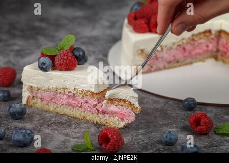 Köstlicher Himbeerkuchen mit Rahm und dekoriert mit frischen Himbeer-Beeren und Minzblättern. Gabel bricht einen Teil des Kuchens ab Stockfoto