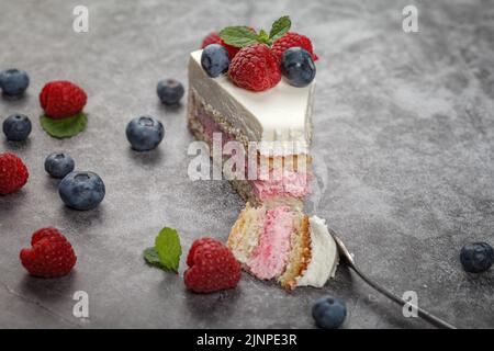 Köstlicher Himbeerkuchen mit Rahm und dekoriert mit frischen Himbeer-Beeren und Minzblättern. Gabel bricht einen Teil des Kuchens ab Stockfoto