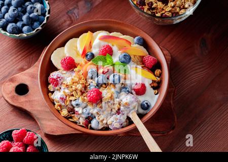 Schüssel mit hausgemachtem Müsli mit Joghurt und frischen Beeren auf Holzboden. Gesundes Frühstück mit Joghurt, Müsli und Obst auf Schneidebrett. Flach Stockfoto
