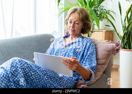 Schöne reife ältere Frau zu Hause, häusliches Leben und Freizeit Momente - 50-60 Jahre alt hübsche weibliche Erwachsene entspannen auf dem Sofa und mit Computer Stockfoto