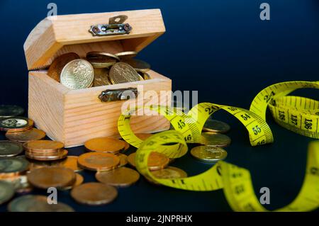 Schatzkiste mit verstreuten Goldmünzen mit Maßband. Gesundheits- und Wohlstandskonzept. Stockfoto