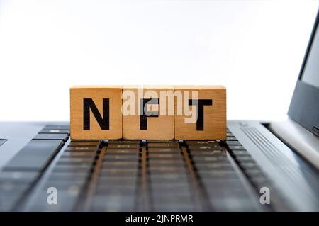 NFT steht für nicht-fungiblen Token-Text auf Holzblöcken auf dem Laptop. Kryptowährungskonzept. Stockfoto