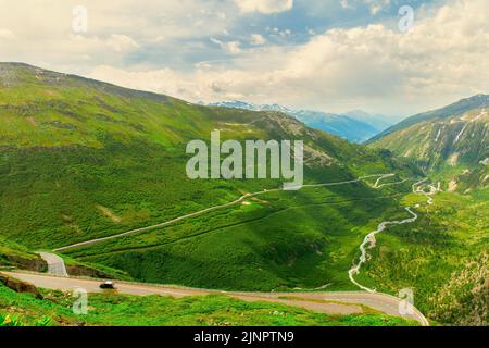 Alpine Berglandschaft. Furka Pass in Schweizer Alpen im Sommer. Eine gewundene Serpentinenstraße windet sich zwischen den grünen Bergen, einem bergigen, schnellen Fluss f Stockfoto