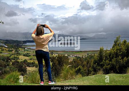 Frau, die an einem bewölkten Tag ein Bild von einem See fotografiert Stockfoto