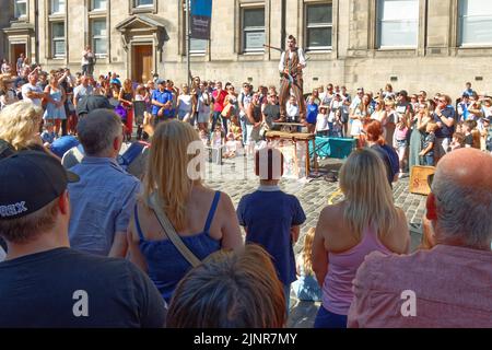 EDINBURGH FESTIVAL FRINGE 2022 ROYAL THE MILE ZUSCHAUER BEOBACHTEN LAUT MIME, WIE SIE BALANCEAKT UND JONGLIEREN MIT MESSERN ZEIGEN Stockfoto