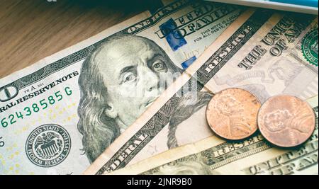 US-Dollar-Scheine und Münzen auf einem Holzmöbel mit einem Rechner in der Zusammensetzung. Finanz- und Wirtschaftskonzepte. Stockfoto